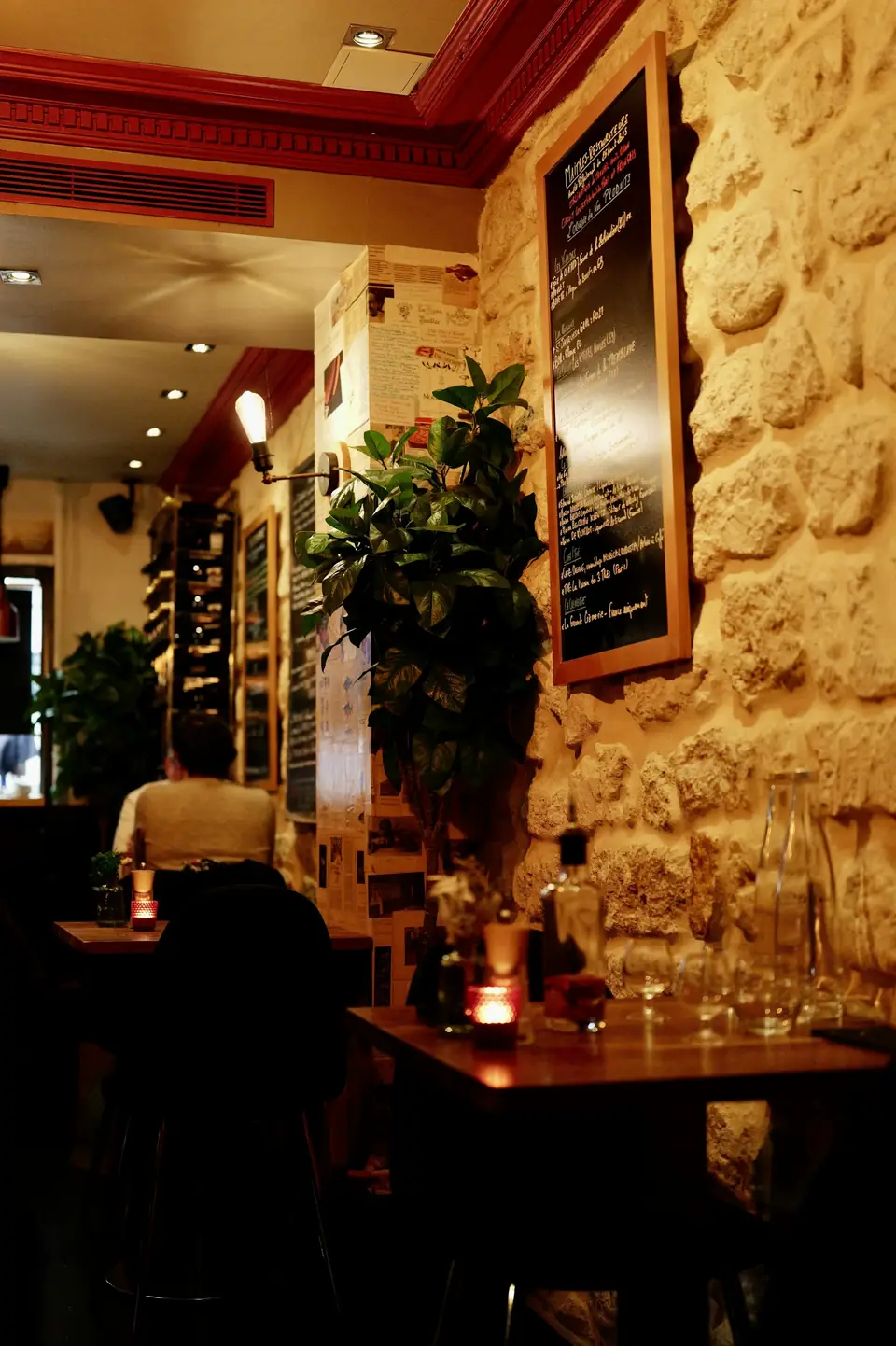 Le Caveau : mur de pierre éclairé à la bougie, ardoise accrochée au mur et petites tables dressées